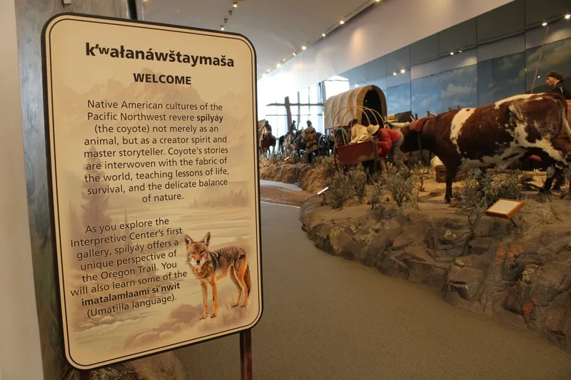 Gallery welcome panel in Umatilla language and English beside a covered-wagon diorama